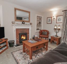 A living room with a fireplace television sofa armchair coffee table and a lamp at Kirkstone Cottage in Ambleside
