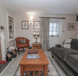 A living room with a fireplace a wooden coffee table a sofa an armchair and a door at Kirkstone Cottage in Ambleside