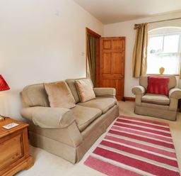 A living room with a beige sofa and armchair a striped red rug and a wooden cabinet with a red lamp at Elder Cottage Mickleton near Chipping Campden