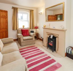 A living room with a beige sofa and armchair a fireplace and a striped rug at Elder Cottage in Mickleton near Chipping Campden
