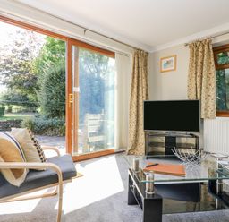 A sitting room with a chair and cushions a glass coffee table and a television near sliding glass doors at Manege Cottage Near St Agnes