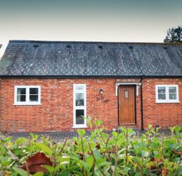 A brick house with a wooden door and multiple windows with a hedge in front at South Lodge in Hazelbury Bryan