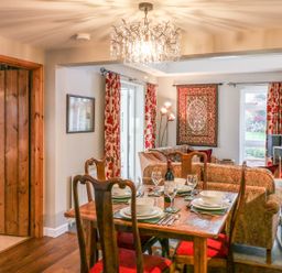 A dining table set with plates glasses and cutlery next to a sitting area with sofas a rug on the wall and a stove with a chimney at South Lodge in Hazelbury Bryan