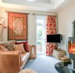 A living room with a leather sofa a wall hanging a standing lamp a wood burning stove and a small TV at South Lodge in Hazelbury Bryan