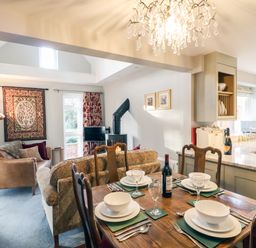 A dining table set with bowls plates glasses and cutlery beside a living area with sofas a wood stove and a kitchen in the background at South Lodge in Hazelbury Bryan