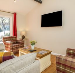 A living room with a sofa and armchairs around a coffee table with flowers and magazines at Zeal Cottage in Crediton