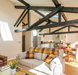 A living room with sofas and a dining table with chairs under exposed wooden beams at Zeal Cottage in Crediton