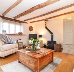 A living room with wooden ceiling beams a wood stove and a coffee table with flowers at Pollys Bower in Landrake