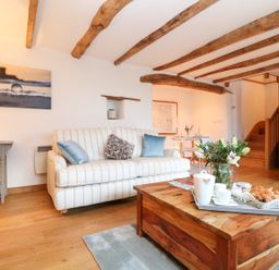 A living room with a striped sofa and wooden coffee table with flowers and breakfast at Polly's Bower in Landrake