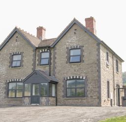 A stone house with two chimneys and dark framed windows surrounded by grass and trees at The Farm in Presteigne