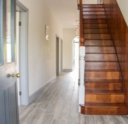 A hallway with wooden stairs and grey tiled floor at The Farm in Presteigne