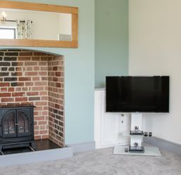 A room with a brick fireplace and a black stove next to a wall-mounted television on a stand at The Farm in Presteigne