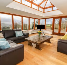 A living room with large windows wooden coffee table and brown sofas at Oakwood House in Rhayader