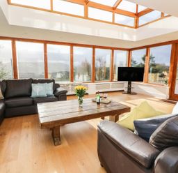 A living room with leather sofas a wooden coffee table and large windows at Oakwood House in Rhayader