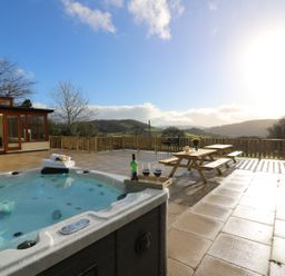 An outdoor patio with a hot tub, wooden picnic tables, and a view of hills at Oakwood House in Rhayader