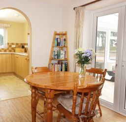 A dining area with a round wooden table and chairs with a vase of flowers by a glass door and a ladder shelf with books at Broadway Lands Farm in Little Dewchurch
