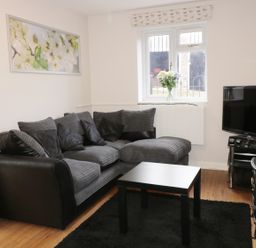 A living room with a gray sectional sofa a black coffee table a television on a stand and a window with flowers at Broadway Lands Farm in Little Dewchurch