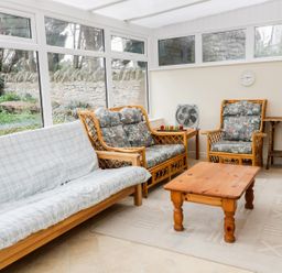 A conservatory with wooden furniture including a sofa, armchair, table, and side table at Broadway Lands Farm in Little Dewchurch