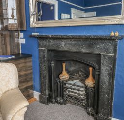 A room with a black fireplace two vases on the hearth and a beige armchair with a cushion at Apartment 3 in Tenby
