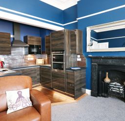 A kitchen with wood cabinets and black fireplace next to brown leather sofa at Apartment 3 in Tenby