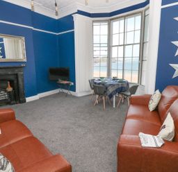 A living room with two brown sofas a small dining table by a bay window and a fireplace at Apartment 3 in Tenby