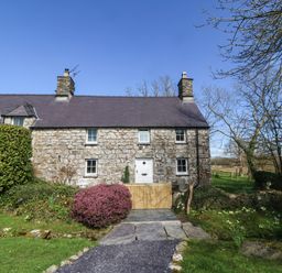 A stone cottage with a wooden gate and bushes in front at Y Bwthyn Ty Du in Pwllheli