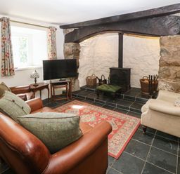 A living room with leather sofas a television and a fireplace with a wood burner at Y Bwthyn Ty Du in Pwllheli