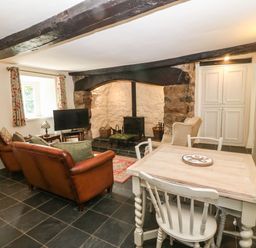 A living room with leather sofas a wood stove a dining table and chairs at Y Bwthyn Ty Du in Pwllheli