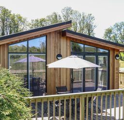 A wooden cabin with large windows and a patio table with an umbrella at Woodpecker Lodge in Gargrave