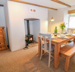 A dining room with a wooden table set for four near a window and a wood burning stove at Blue Anchor in Fraddon