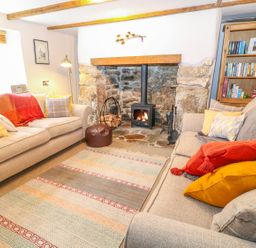 A living room with two sofas a stone fireplace with a wood burning stove a bookshelf and a rug at Blue Anchor in Fraddon