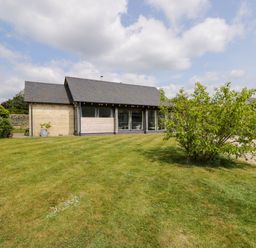 An exterior view of a single-story house with a lawn and a tree in front at The Barn at Daubeneys in Colerne