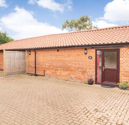 Brick building with a tiled roof and a brown door with plants on a paved area at The Hen House in Diss near Gissing