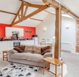 An open plan living space with a kitchen and dining area including a beige sofa with cushions and wooden beams at The Hen House in Diss near Gissing