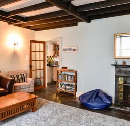A living room with a leather sofa an armchair a wooden coffee table a bookshelf and a fireplace at Tower House in Boscastle