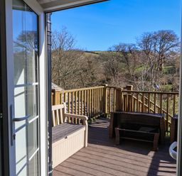 A balcony with a wooden bench and table set overlooking trees and hills at Tower House in Boscastle