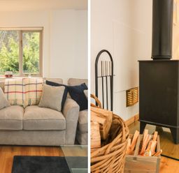 A living room with a beige sofa with cushions and a blanket a window and a lamp next to a black wood stove with firewood and kindling at Cross Syke Barn in Loxhore near Barnstaple