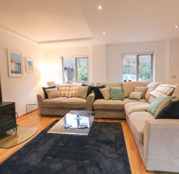 A living room with beige sofas and cushions a black wood stove and a glass coffee table at Cross Syke Barn in Loxhore near Barnstaple