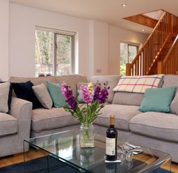 A living room with a glass coffee table a vase of flowers a bottle of wine and a sectional sofa at Cross Syke Barn in Loxhore near Barnstaple