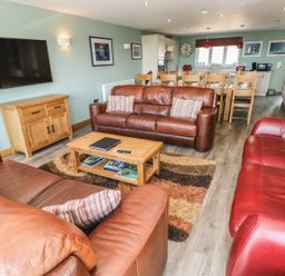 A living room with leather sofas a wooden coffee table and a dining table with chairs at Harmon Vale in Solva