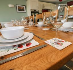 A dining table set with white bowls, plates, wine glasses, cutlery and poppy flower placemats in a kitchen at Harmon Vale in Solva
