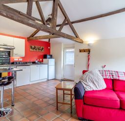 A kitchen and living area with wooden beams white cabinets red wall and red sofa at The Nest Box in Diss