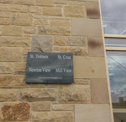 A stone wall with a sign listing St Dolmen St Cruz Newton View and Mill View next to a glass and metal staircase at St Dolmen in Embleton