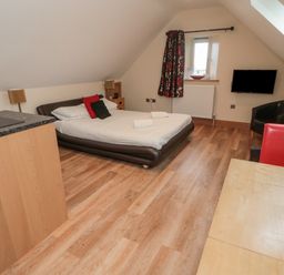 A bedroom with a bed a small wooden cupboard a wall-mounted television a black chair and a table with a fruit bowl at St Dolmen in Embleton