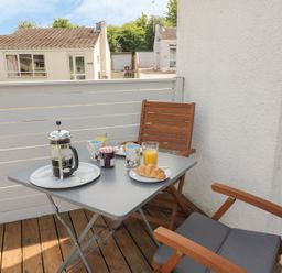 A small balcony with a table set for breakfast with coffee, croissants, jam, orange juice and wooden chairs at 54 The Moorings in St Dogmaels