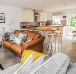 A kitchen with cream cabinets and wooden countertops next to a living area with a brown leather sofa and a patterned sofa at 54 The Moorings in St Dogmaels