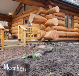A wooden log cabin with a small porch and railing and a rock with Moorhen written on it at Moorhen Lodge in North Kessock