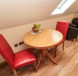 A wooden round table with a bowl of fruit and two red chairs in a room with wood flooring and a skylight window at St Cruz in Embleton