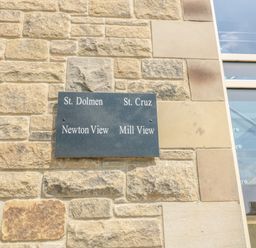 A stone wall with a black plaque listing St Dolmen St Cruz Newton View and Mill View at Newton View in Embleton