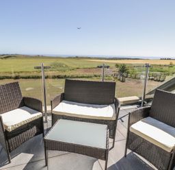 An outdoor seating area with two armchairs a loveseat and a glass-top table on a balcony with a view of fields at Mill View in Embleton